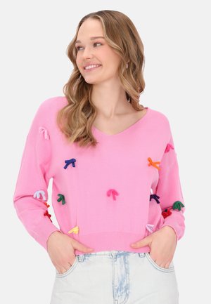 Różowy sweter z dekoltem w serek i długimi rękawami, z wielokolorowymi aplikacjami w kształcie kokard na całej przedniej części oraz ściągaczem u dołu.