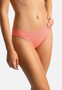 Bas de bikini côtelé corail avec une taille basse, présentant une ceinture sans couture et une texture lisse. Idéal pour les collections de maillots de bain.