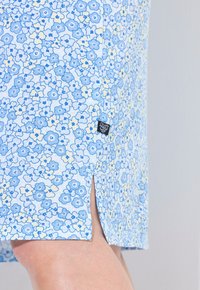 Abito con stampa floreale in azzurro chiaro e crema, caratterizzato da uno spacco laterale, realizzato in tessuto morbido con un piccolo etichetta sull'orlo.