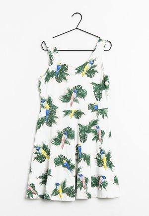 Vestido blanco sin mangas con escote redondeado, decorado con hojas tropicales verdes y loros de colores, colgado en una percha negra.