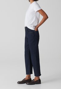 Maglietta bianca a maniche corte abbinata a jeans a vita alta in denim scuro, dal taglio rilassato, con tasche laterali e orli rifiniti. Indossati con mocassini marroni.