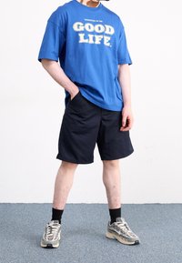 Blue short-sleeve t-shirt with white text reading "GOOD LIFE," paired with navy shorts and gray sneakers with white accents.