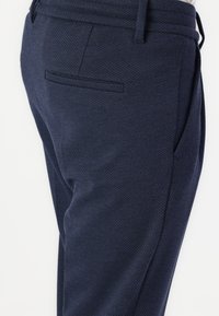 Pantalones de tela azul marino con un corte recto, que cuentan con bolsillos laterales y un bolsillo trasero para mayor utilidad. Incluye detalles en la cinturilla a medida.