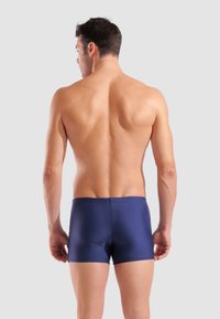 Marineblaue Badehose mit glatter Textur und elastischem Bund, entworfen für einen figurnahen Stil, von hinten auf einem neutralen Hintergrund gezeigt.