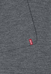 Tissu gris tricoté avec un détail de couture visible et une petite étiquette rouge Levi's sur le bord du matériau.