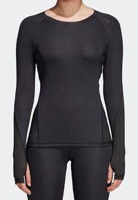 Svart långärmad träningsöverdel av elastiskt tyg, med raglanärmar och tumhål i ärmsluten för extra skydd.