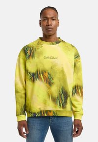 Farverig sweatshirt i lys gul med abstrakte grønne og orange mønstre. Har en rund hals og ribbede manchetter. Logo på brystet.