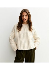 Maglione lavorato a maglia color crema con motivo testurizzato in rilievo e scollatura rotonda. Presenta maniche lunghe e una vestibilità rilassata. Abbinato a pantaloni color oliva.