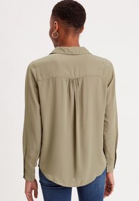 Chemise à manches longues vert olive avec un pli souple dans le dos, un ourlet arrondi et des poignets boutonnés, confectionnée dans un tissu lisse et léger.