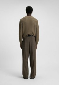 Knit, olive-colored sweater with a textured diamond pattern, paired with brown plaid trousers, loose-fit, and black belt.
