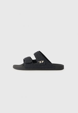 Svart tyg slide-sandal med två velcro-remmar och en svart gummisula. Har en liten metallisk logotypdetalj på ena sidan.