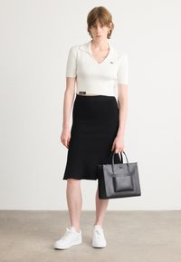 Weißes geripptes Polo-Shirt mit kurzen Ärmeln, schwarze gerippte Midirock, weiße Sneakers und eine schwarze Lederhandtasche mit zwei Griffen.
