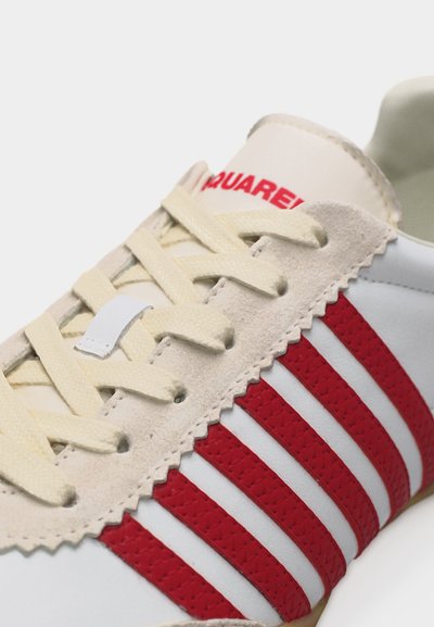 Λευκό αθλητικό παπούτσι με κόκκινες ρίγες, μπεζ σουέτ περιοχή κορδονιών, μπεζ κορδόνια και κόκκινο κείμενο "SQUARE!" στη γλώσσα.