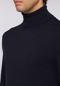 Dolcevita blu realizzato in tessuto a maglia fine. Presenta un colletto a coste e un logo ricamato discreto sul petto.