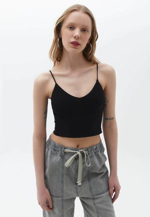 Black ribbed crop top with thin adjustable straps and a V-neckline, paired with light gray drawstring waist pants in a relaxed fit.
