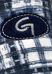 Tela de denim con un patrón de cuadros en tonos azul marino y blanco, que presenta un parche ovalado azul con costuras blancas y un logo estilizado de "G".