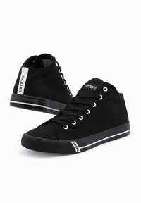 Zapatillas altas negras de lona con ojales blancos, suela de goma a rayas y un acento de logo en el lateral.