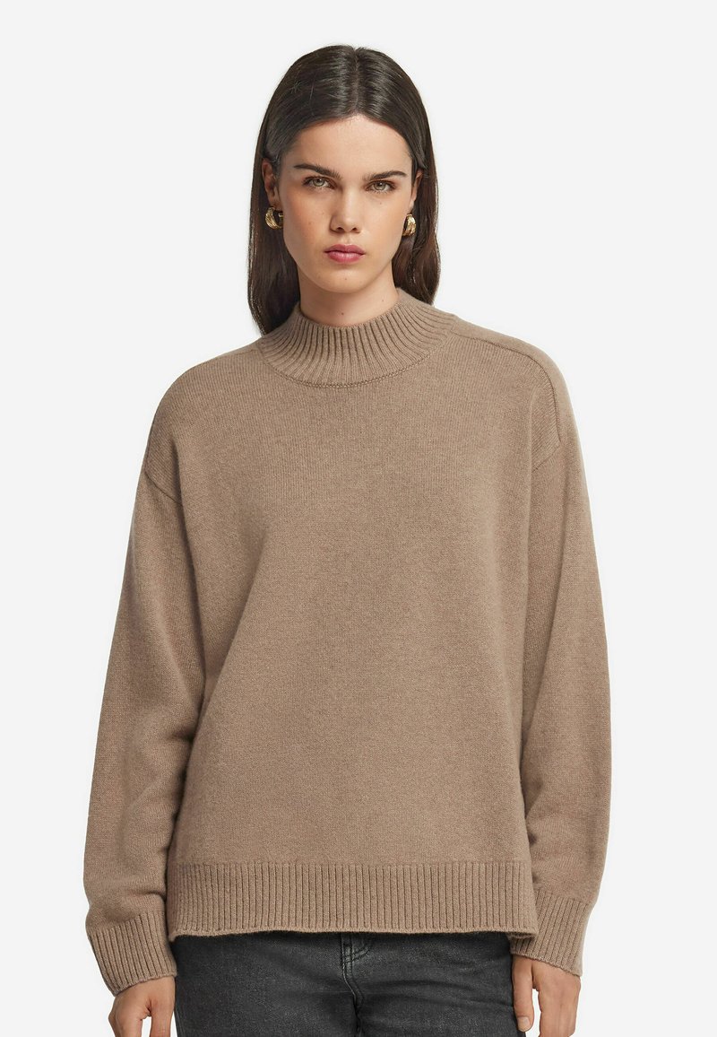 Beige Strickpullover mit hohem Rippkragen, lockerer Passform und gerippten Bündchen. Weiche Textur, minimale Nähte und keine Verzierungen.