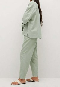 Světl zelená oversized bunda a odpovídající zúžené kalhoty vyrobené z měkké tkaniny. Sandály s bílými popruhy a neutrální podrážkou doplňují tento outfit.