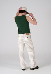Green ribbed sleeveless top paired with ivory striped trousers. The trousers have a subtle texture and a brown leather patch on the back.