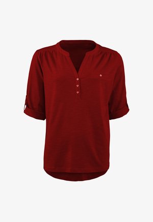 Rote kurzärmelige Bluse mit Henley-Ausschnitt, die drei Knöpfe, eine kleine Brusttasche und aufgekrempelte Ärmel aufweist. Weicher, leichter Stoff.