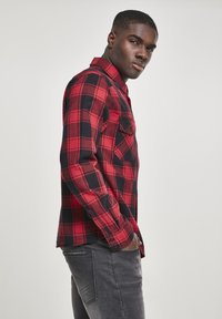 Rood en zwart geruite flanellen overhemd met knoopsluiting aan de voorkant, lange mouwen en één zak, gecombineerd met grijze jeans.