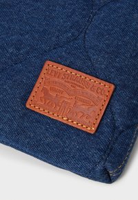 Écusson en cuir marron Levi Strauss & Co cousu sur un tissu en jean bleu montrant des coutures détaillées et un logo de cheval embossé.