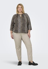 Bluza s leopardjim vzorcem, okroglim izrezom in odprtino na hrbtu, v kombinaciji z svetlo bež hlačami. Obutev so črne loferice.