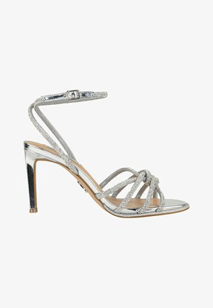 Sandal con tacco alto argento con finitura metallica lucida, cinturini glitterati, fibbia alla caviglia e un tacco sottile. Presenta un design incrociato.