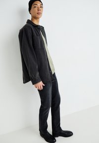 Juodas džinsinis marškinis su priekinėmis kišenėmis, apsivilktas šviesiai žaliu marškinėliu. Visiškai derinami siauri juodi džinsai ir juodi aulinukai.