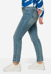 Ljusblå slim-fit jeans med en slät textur. Har fem fickor och diskret sömnad. Matchas med vita sneakers.