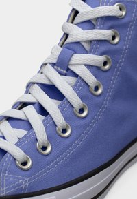 Αθλητικό παπούτσι με ψηλό πάτο, με επάνω μέρος από ανοιχτό μπλε καμβά, λευκά κορδόνια, μεταλλικά οπές και μαύρη ελαστική σόλα. Διακρίνονται υφή υφάσματος και ραφές.