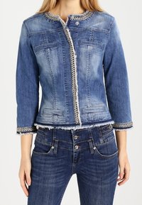 Giacca di jeans con lavaggio azzurro chiaro, design corto, rifinitura decorativa con catena e due tasche frontali. Abbinata a jeans blu simili.