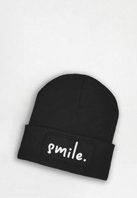 Black knit beanie with ribbed texture, featuring a rectangular patch that displays the word "smile." in bold white lettering.