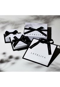 Vier rechteckige Geschenkschachteln in Weiß mit schwarzen Deckeln, ausgestattet mit schwarzen Bändern und der "LATELITA"-Marke auf jeder Box. Verschiedene Größen, glatte Oberfläche.