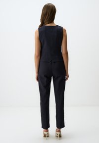 Gilet su misura a righe navy e pantaloni affusolati, realizzati in tessuto testurizzato, con uno spacco sul retro e abbinati a tacchi di colore chiaro.