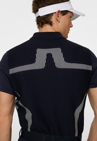 Marinblå golfpolo med ribbad textur och vitt randmönster över ryggen. Korta ärmar med kontrasterande tyg på axlarna.