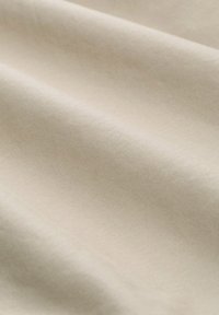 Beige Stoff mit einer glatten, leicht strukturierten Oberfläche, die weiche Falten zeigt und eine einheitliche, helle Farbe mit subtilen Variationen aufweist.