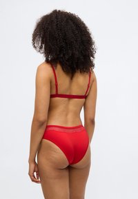 Rød bh med blondekant og højtaljede trusser, lavet af glat stof. Justerbare stropper på bh'en med en simpel spænde.