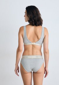 Szürke pamut bralette, alacsony hátrész és állítható kampós záródás; hozzáillő szürke bugyi bézs derékkal, amelyen a Calvin Klein logó található.