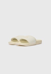 Cream-colored slip-on sandals with a perforated upper, flat sole, and a rounded toe design. Lightweight and minimalistic.