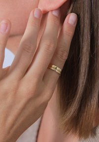 Golden rings stacked on a finger, featuring a smooth band, textured and patterned accents, against a background of skin and hair.