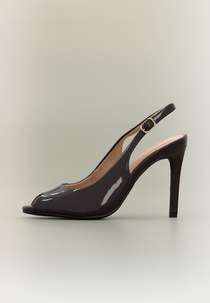Escarpin ouvert à bout ouvert en cuir verni noir avec une fine bride à la cheville et une boucle dorée sur un fond neutre.