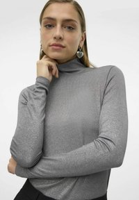 Pull gris à col montant avec texture côtelée et manches longues, fabriqué à partir d'un tissu métallique qui capte la lumière.