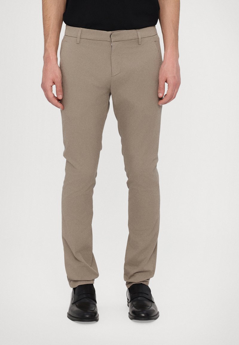 Slim-fit beige byxor gjorda av strukturerad tyg med dragkedja i gylfen, sidofickor och bärs med svarta dressade skor.