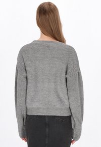 Grå strikket sweater med en løs pasform, brede lange ærmer og en ribbet halsudskæring. Stoffet ser blødt ud med en tekstureret finish.
