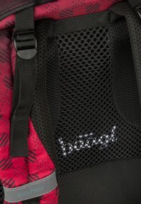 Černo-červený batoh s prodyšným zadním panelem, nastavitelnými popruhy a logem; na látce jsou viditelné geometrické vzory.