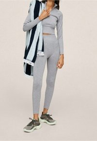 Completo sportivo grigio composto da una maglietta a maniche lunghe cropped e leggings a vita alta. Accompagnato da un asciugamano a righe blu e navy. Sneakers scure.