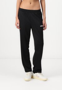Fekete sportnadrág sima anyagból, rugalmas derékkal. Bal combon fehér Adidas logóval rendelkezik. Egyenes lábú dizájn.