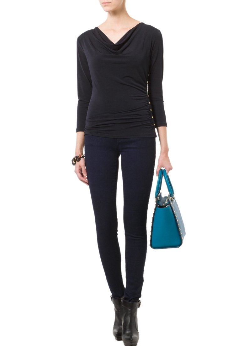 Top negro de manga larga con escote drapeado y detalles gather en el lateral, combinado con jeans skinny azul oscuro y un bolso turquesa.